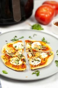 air fryer margherita pizza cut in 4 slices on a wite plate sprinkled with fresh herbs