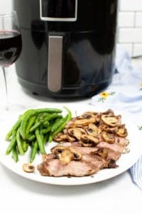 Steak and Mushrooms on a white plate with green beans. An Air Fryer is in the background.