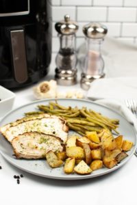 Plate of seasoned turkey breast with beans and potatoes with air fryer in background