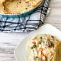 Chicken Pot Pie on a white plate with pan of whole pot pie in the background on a blue plaid cloth