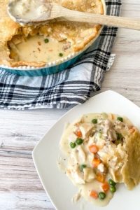 Chicken Pot Pie on a white plate with pan of whole pot pie in the background on a blue plaid cloth