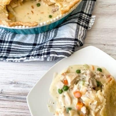 Chicken Pot Pie on a white plate with pan of whole pot pie in the background on a blue plaid cloth