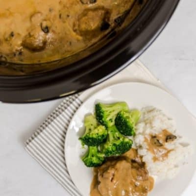 Salisbury steak on a white plate with a side of broccoli and mashed potatoes