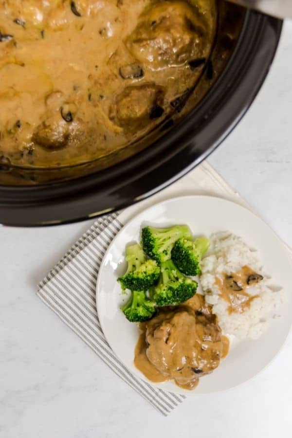 Salisbury steak on a white plate with a side of broccoli and mashed potatoes