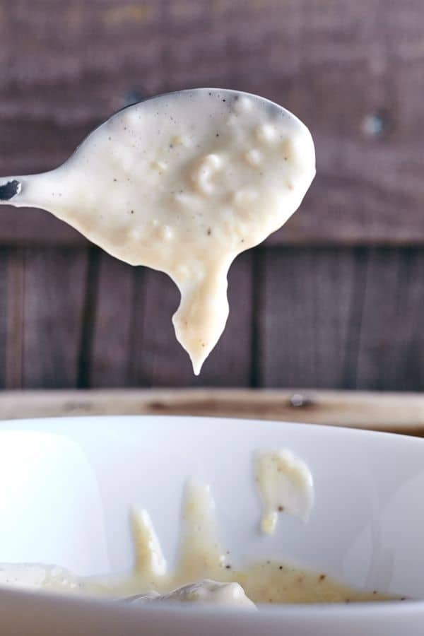Spoon holding Garlic aioli above a white bowl