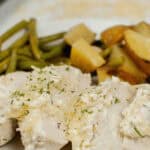 A plate featuring Sheet Pan Chicken with Vegetables, topped with creamy sauce and garnished with herbs. Accompanied by perfectly roasted potatoes and crisp green beans.