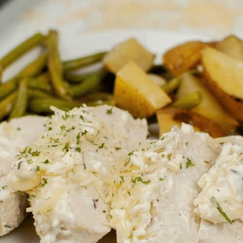 A plate featuring Sheet Pan Chicken with Vegetables, topped with creamy sauce and garnished with herbs. Accompanied by perfectly roasted potatoes and crisp green beans.