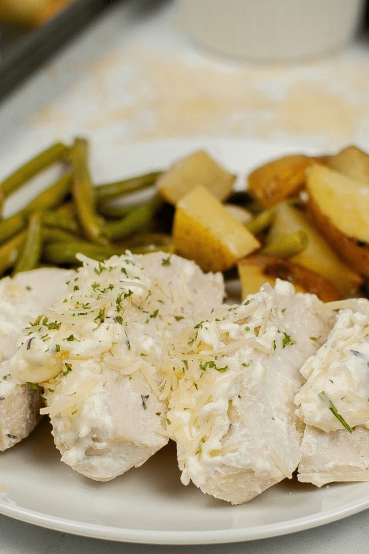 A plate featuring Sheet Pan Chicken with Vegetables, topped with creamy sauce and garnished with herbs. Accompanied by perfectly roasted potatoes and crisp green beans.