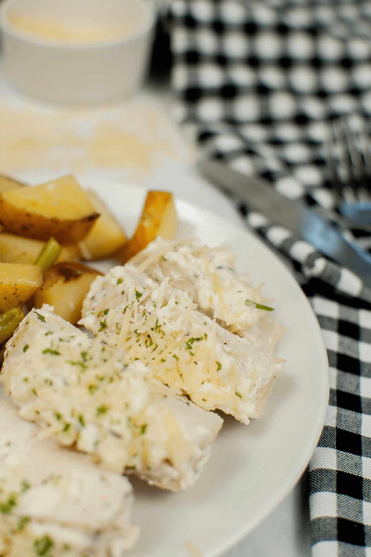 A plate of creamy pasta, topped with herbs and grated cheese, sits invitingly next to roasted potato wedges on a black and white checkered tablecloth. It's the perfect companion to a delightful evening featuring sheet pan chicken with vegetables.