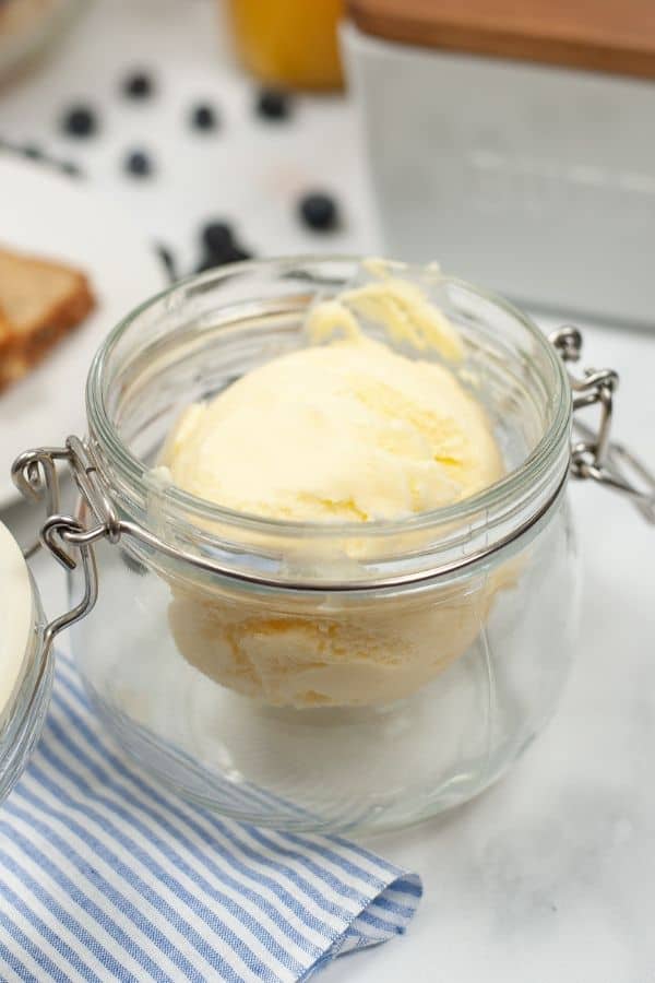 Side view of homemade butter in a jar with bread in the background.
