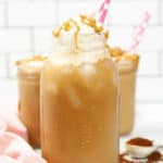 Three Iced Caramel Macchiatos topped with whipped cream and caramel drizzle, served in mason jars with pink and white polka-dot straws.