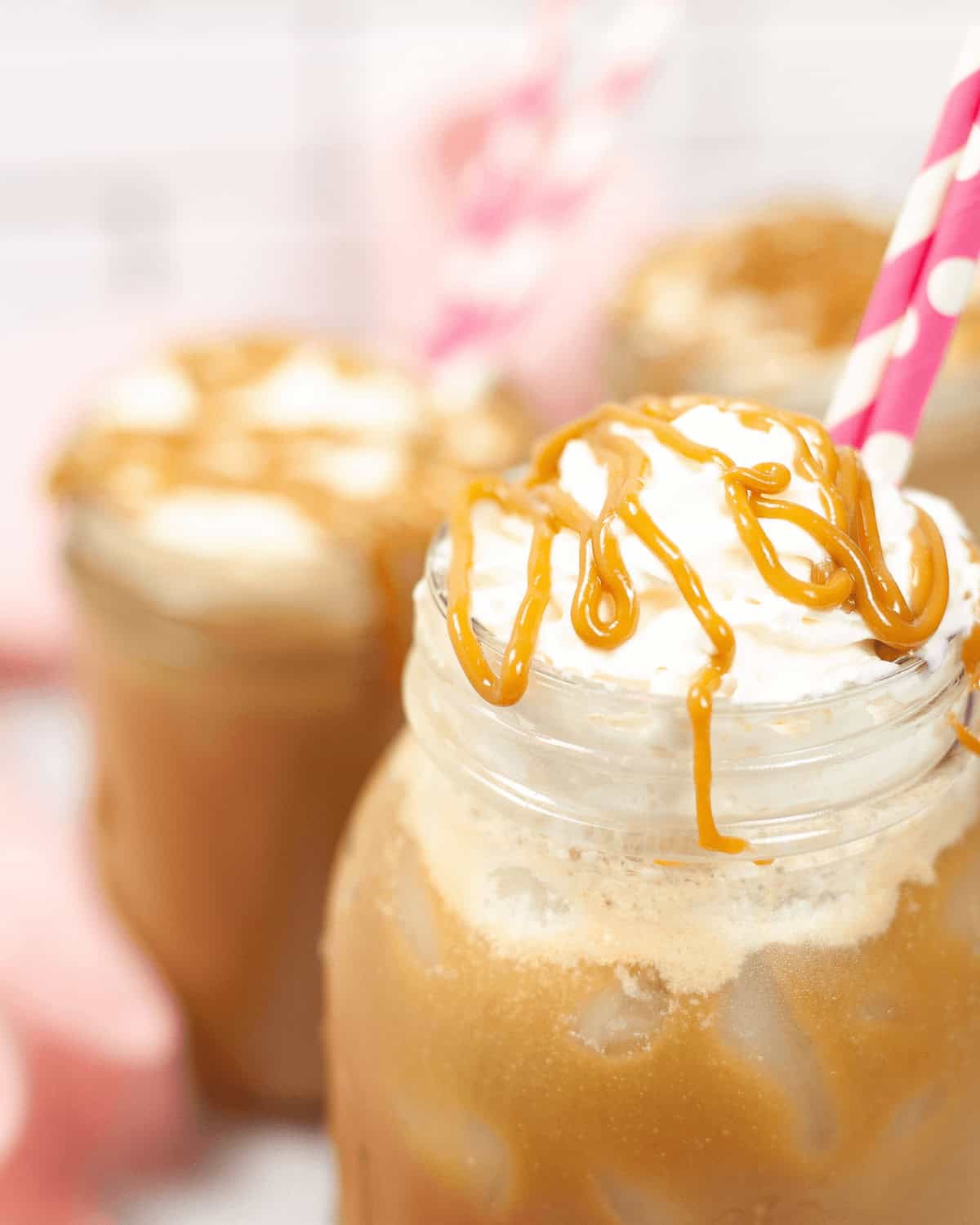 Close-up of three mason jars filled with coffee  caramel drizzle, each with a pink-striped straw.