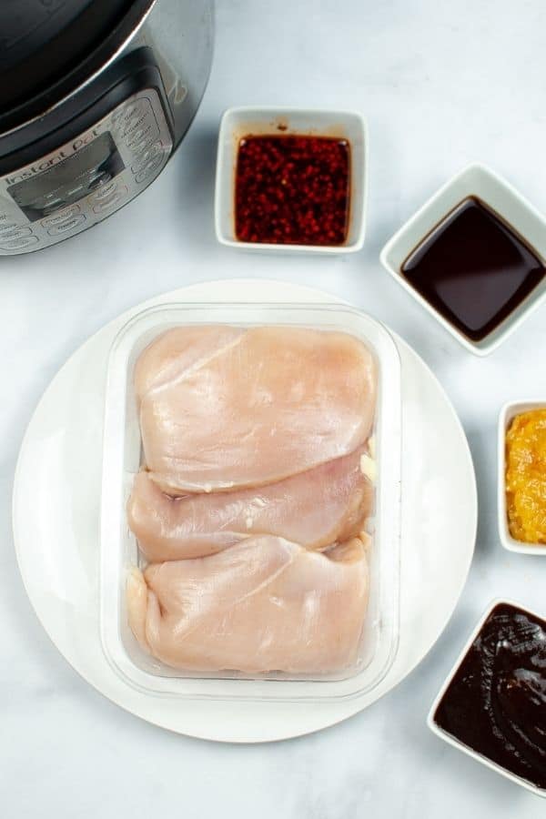 Chicken breast on a white plate with orange marmalade and other ingredients surrounding it in square dishes