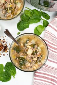 Top shot of Instant Pot Sausage and spinach soup with spinach and Instant pot in backgroup