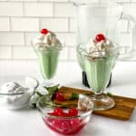 two shamrock shakes on a wood board with bowl of icecream and cherries on front