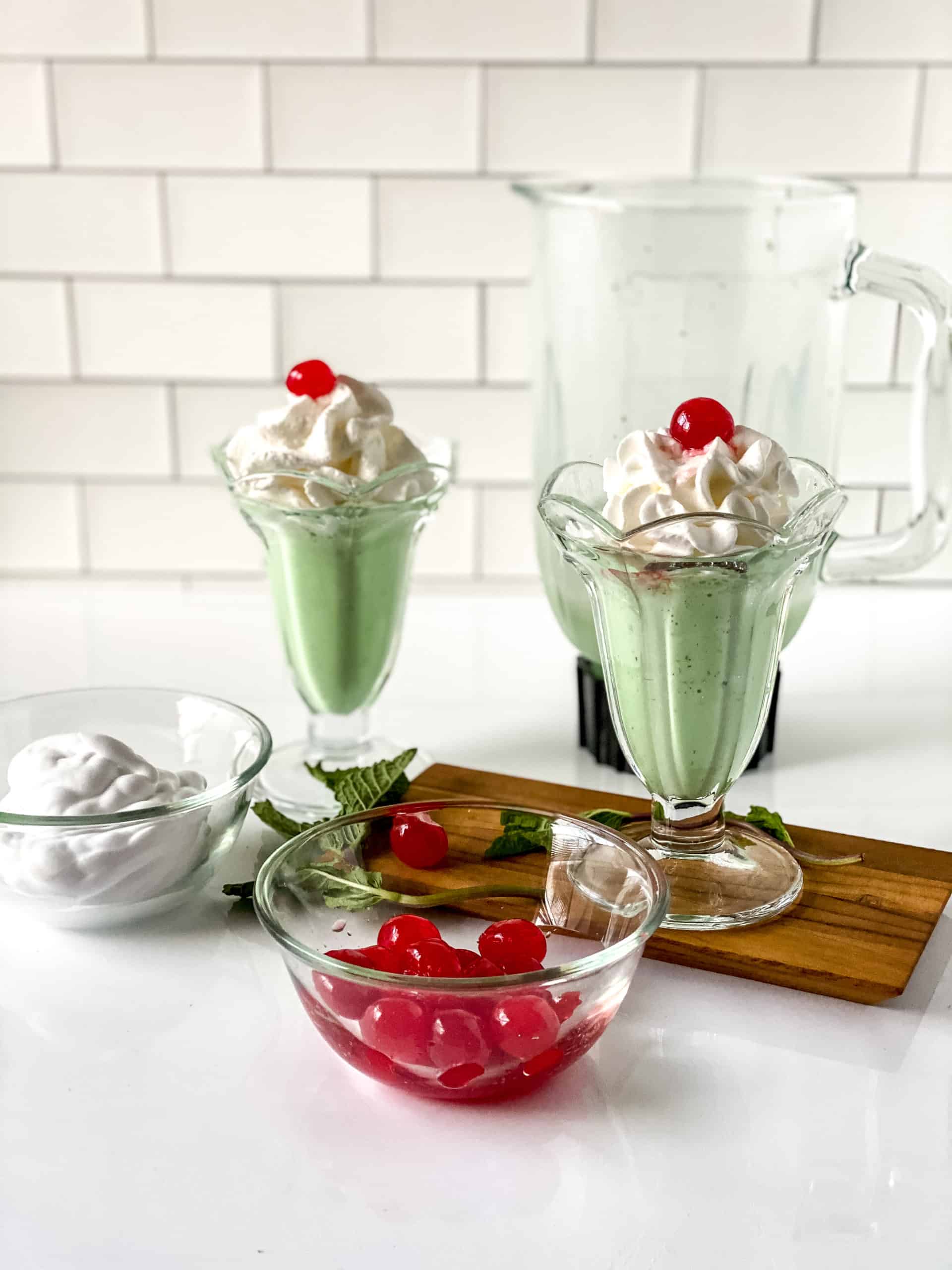 two shamrock shakes on a wood board with bowl of ice cream and cherries on front