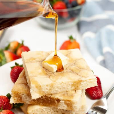 Sheet Pan Pancakes with butter and strawberries, with syrup being poured on them
