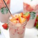 Pink Drink on a white dish with starbucks cups filled with drink in background with whole stawberries.
