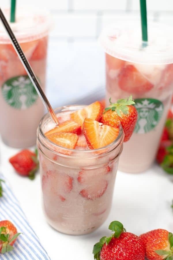 Pink Drink on a white dish with starbucks cups filled with drink in background with whole stawberries.