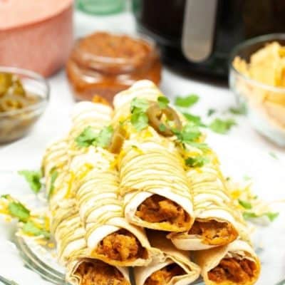 Six Air Fryer Chicken Taquitos stacked on a plate with fresh herbs on top.