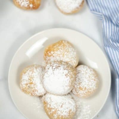 Five deep fried oreos on a plate sprinkled with powdered sugar with a blue and white check napkin.
