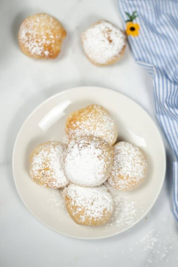 Five deep fried oreos on a plate sprinkled with powdered sugar with a blue and white check napkin.