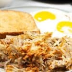 A plate with crispy air fryer hash browns, two sunny-side-up eggs, and a slice of toasted bread.