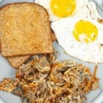 A plate with two slices of toasted bread, two sunny-side-up eggs, and a serving of crispy Air Fryer Hash Browns.