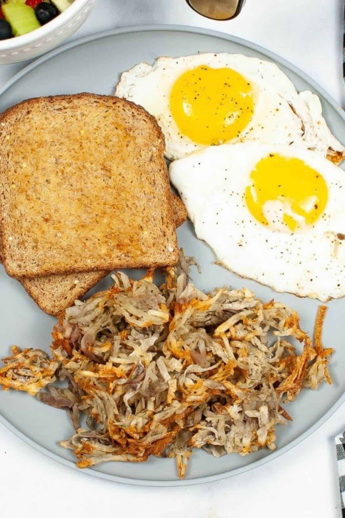 A plate with two slices of toasted bread, two sunny-side-up eggs, and a serving of crispy Air Fryer Hash Browns.
