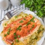 A plate of baked chicken breast topped with paprika and parsley is served over rice and broccoli, reminiscent of a Chicken Broccoli Casserole, with a fork, salt and pepper shakers, and fresh parsley nearby.