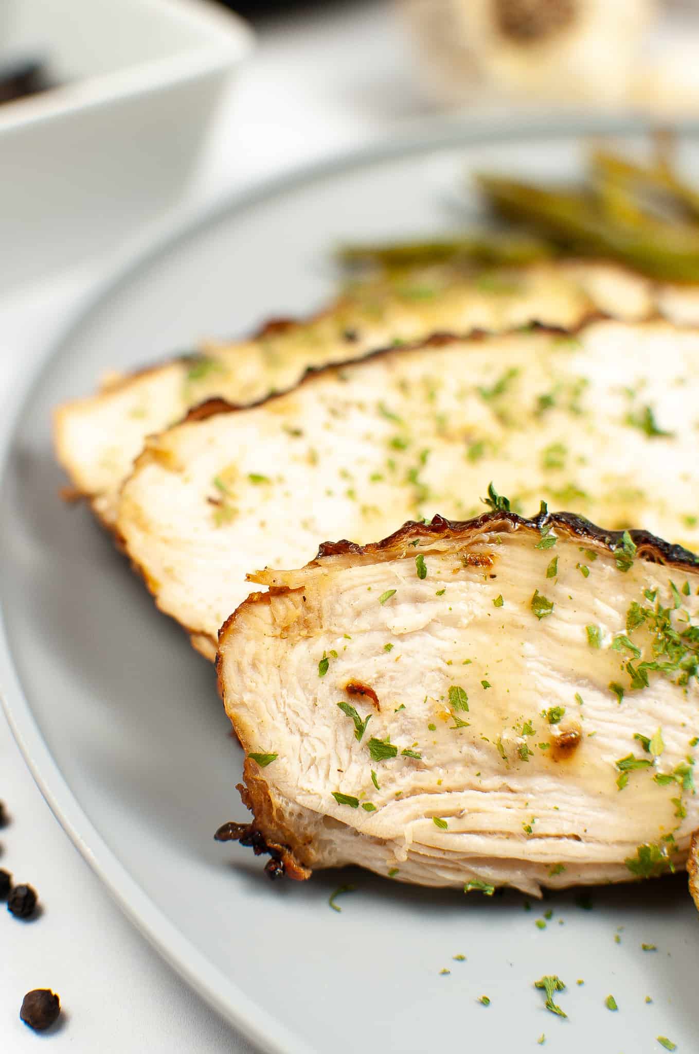 Turkey slices on a white plate with herbs on it and peppercorns on the side.