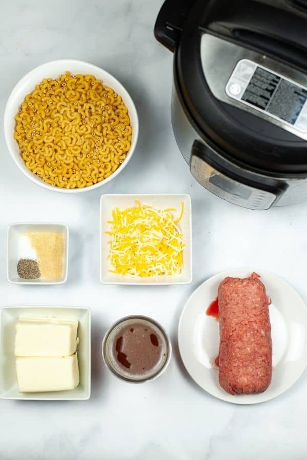 An instant pot surrounded by hamburger, cheese pasta and seasonings.