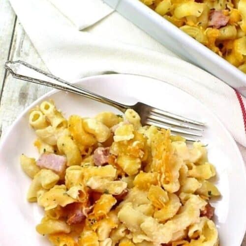 A plate of the mac and cheese with ham with a fork and a napkin.