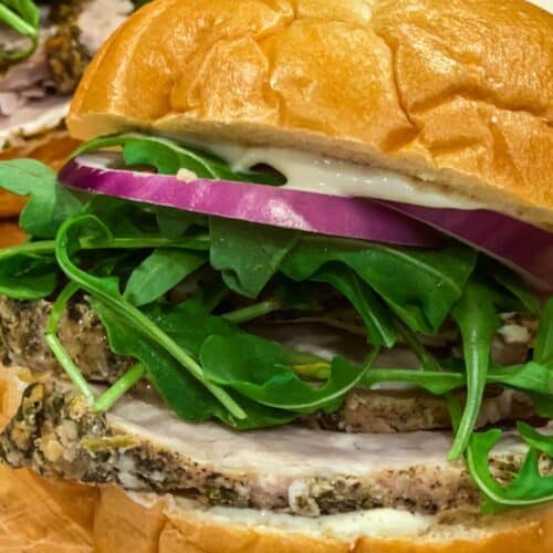 A stacked porchetta sandwich filled with red onion and arugula.