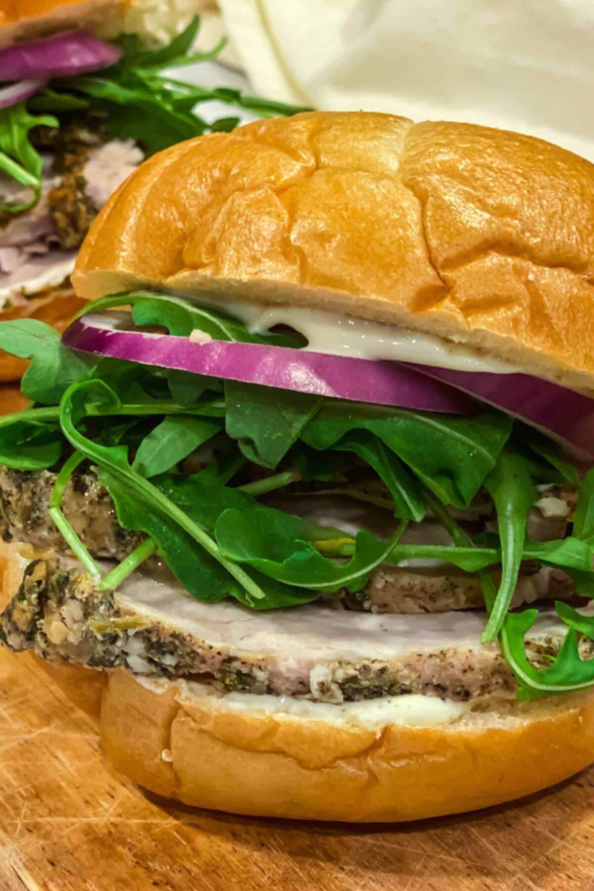 A stacked porchetta sandwich filled with red onion and arugula. 