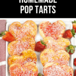 Homemade heart-shaped pop tarts with pink frosting and white sprinkles rest on a white platter, beautifully garnished with fresh strawberries.