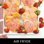 Homemade heart-shaped pop tarts adorned with strawberry frosting and sprinkles rest on a tray, surrounded by fresh strawberries.