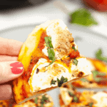A hand holding a slice of Pizza Margherita topped with cheese, tomato sauce, and fresh basil, with more delightful slices on a plate in the background.