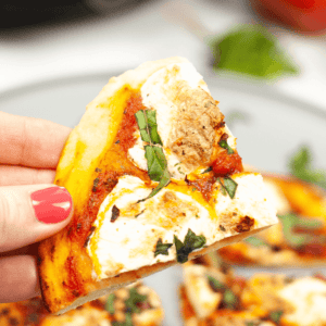 A hand holding a delicious slice of Pizza Margherita with creamy cheese, tomato sauce, and fresh basil on top.