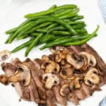 Sliced meat with mushrooms and a side of green beans on a white plate.