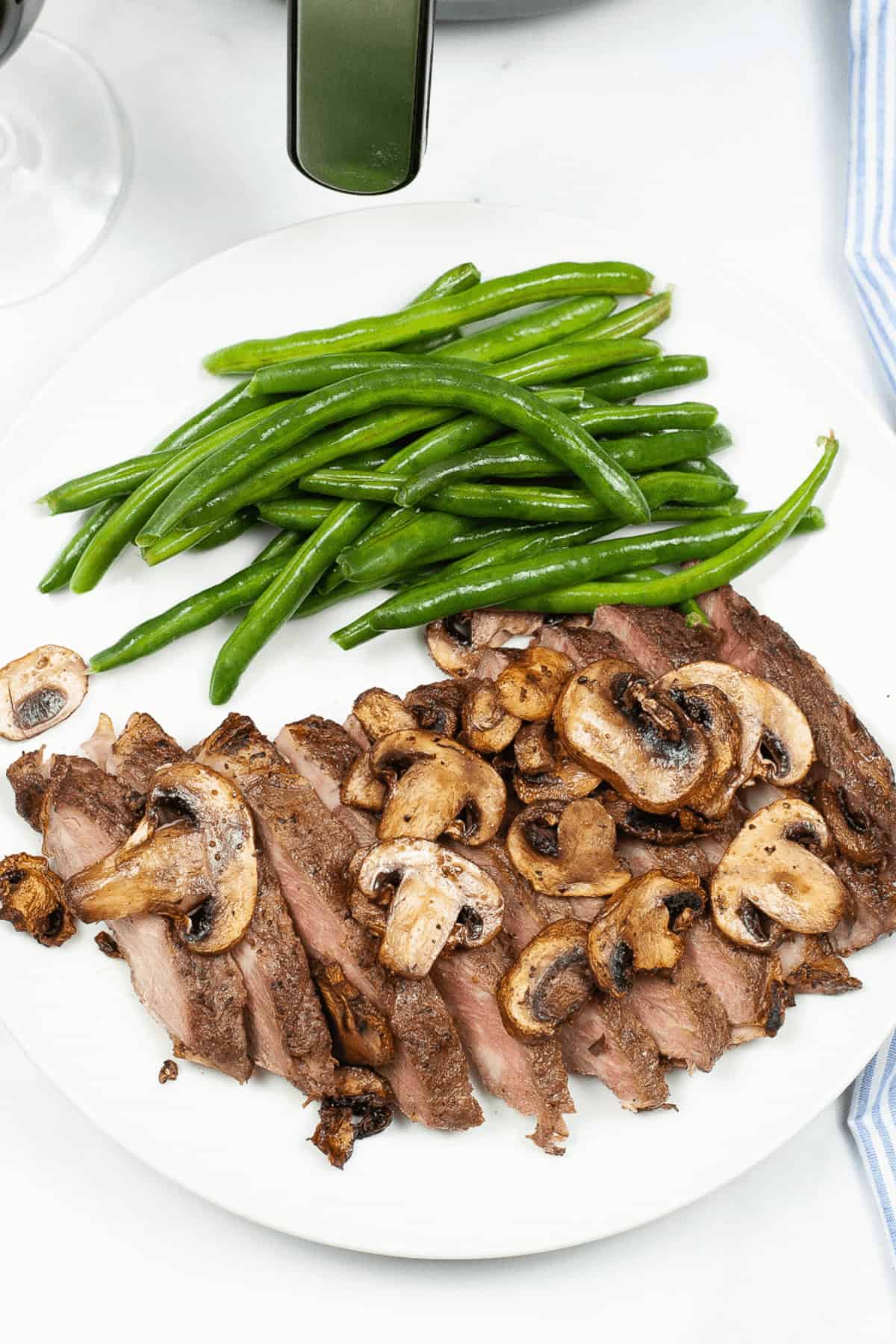 Sliced meat with mushrooms and a side of green beans on a white plate.