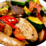 A delightful bowl of cooked vegetables and sliced chicken apple sausage features bell peppers, zucchini, and mushrooms.