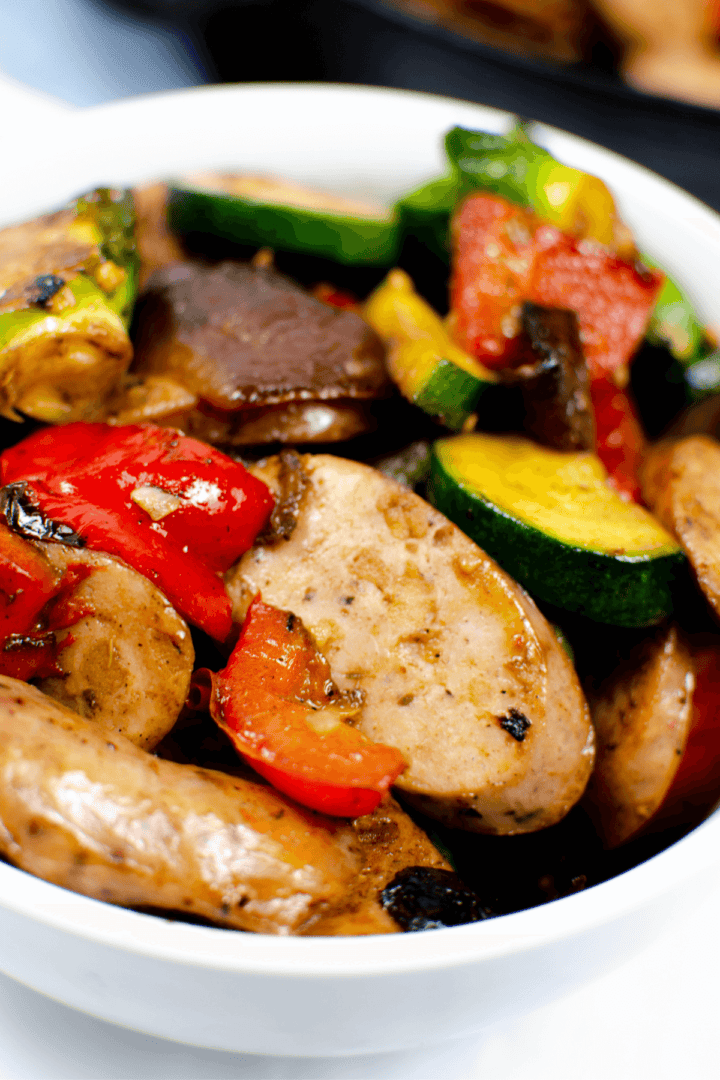A delightful bowl of cooked vegetables and sliced chicken apple sausage features bell peppers, zucchini, and mushrooms.