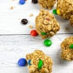 Oatmeal clusters with colorful candy-coated chocolates on a white wooden surface.