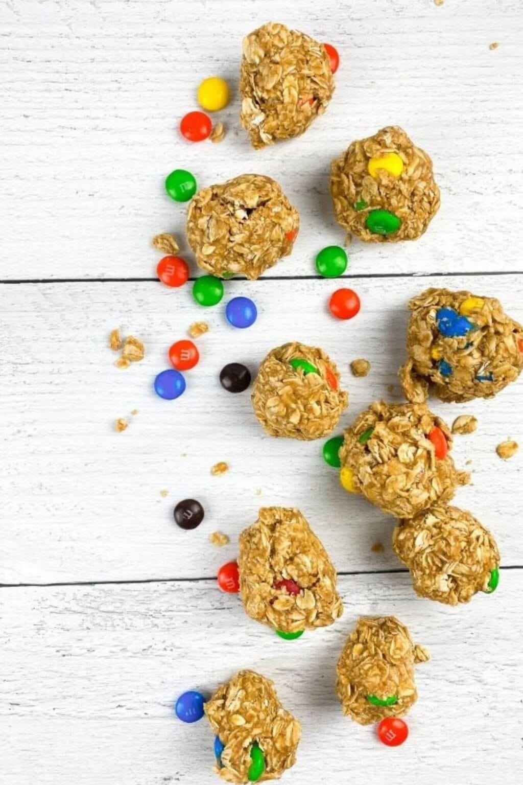 Chocolate Peanut Butter Protein Balls and oatmeal energy bites with colorful candy-coated chocolate pieces are scattered on a white wooden surface.