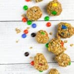 Chocolate Peanut Butter Protein Balls and oatmeal energy bites with colorful candy-coated chocolate pieces are scattered on a white wooden surface.