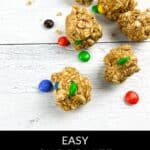 Oatmeal protein balls with chocolate candy pieces scattered on a white wooden surface, showcasing delicious Chocolate Peanut Butter Protein Balls. Text reads "Easy Chocolate Peanut Butter Protein Balls.