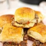 Stack of Instant pot Cheesesteak sliders on a white plate on a white tablecloth.