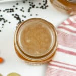 Top view of a jar filled with liquid, surrounded by a striped cloth, black peppercorns, and bay leaves, suggesting a homemade concoction of Instant Pot Chicken Bone Broth preparation.