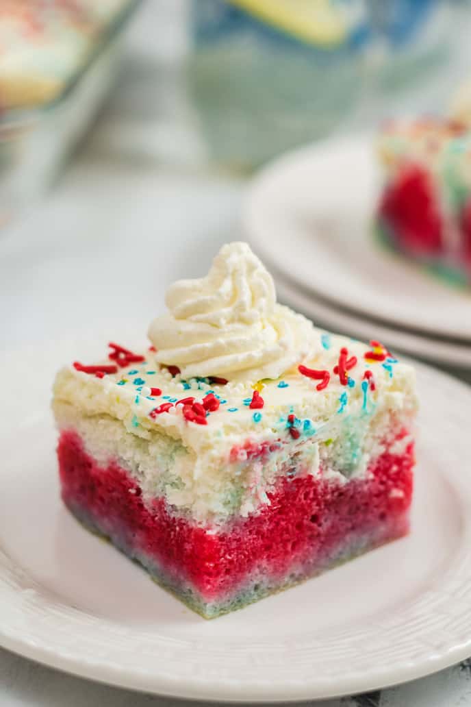 Patriotic Poke Cake Square with sprinkles and whipped cream on a white plate.